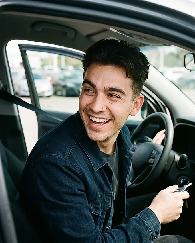 Young man smiling with car keys in vehicle – AI-generated image for car dealership and driving school.