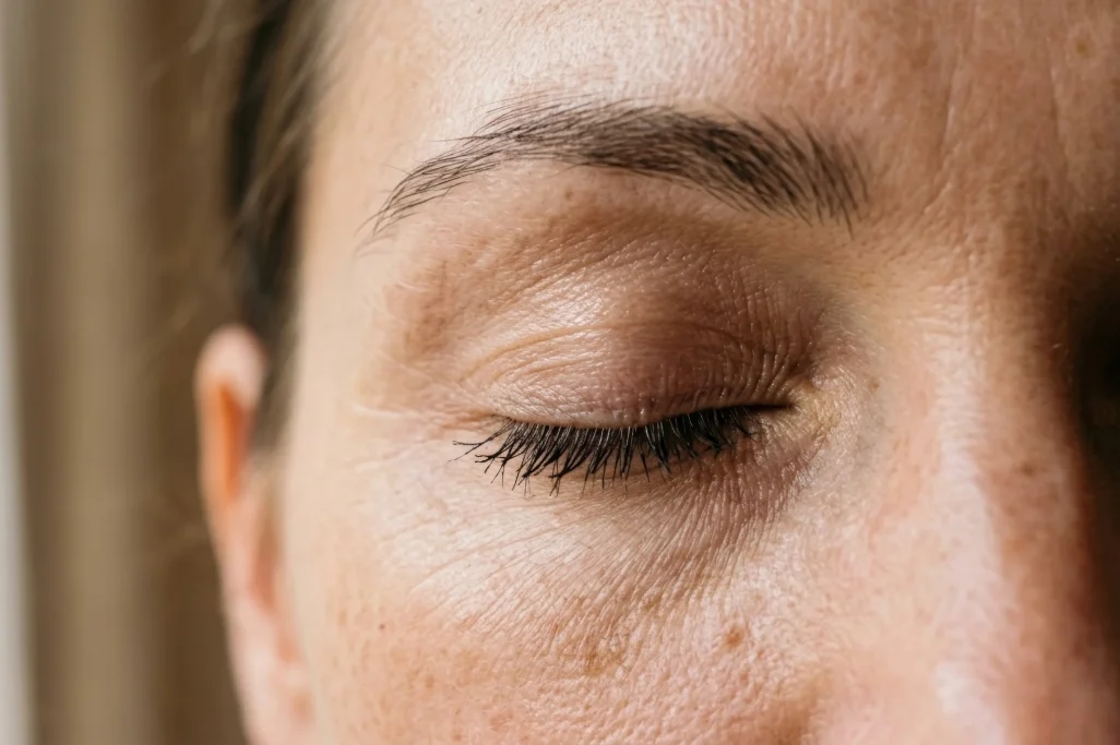 Close-up of a woman's face with eyes closed and freckled skin, in soft natural window light – AI ad image for beauty and skincare brands.