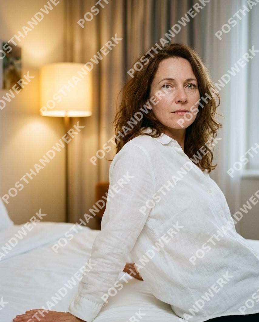 Frau sitzt nachdenklich auf Hotelbett im warmen Lampenlicht – KI-Werbefoto von Posthandwerk für Hotels, Wellness und Übernachtung.